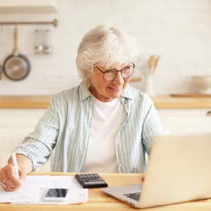 Une personne âgée calcule des éléments à l'aide d'un ordinateur et d'une calculatrice