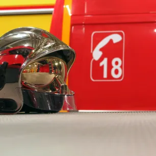 Photographie d'un casque de pompier avec, à l'arrière-plan, la carrosserie d'un camion de pompier et le numéro des secours.