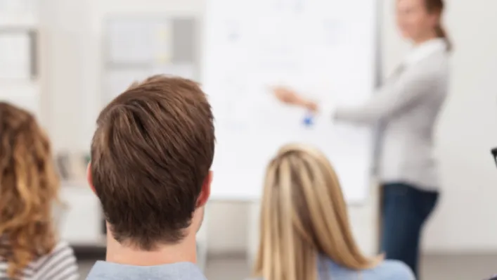 photo de personnes qui écoute une dame devant un tableau